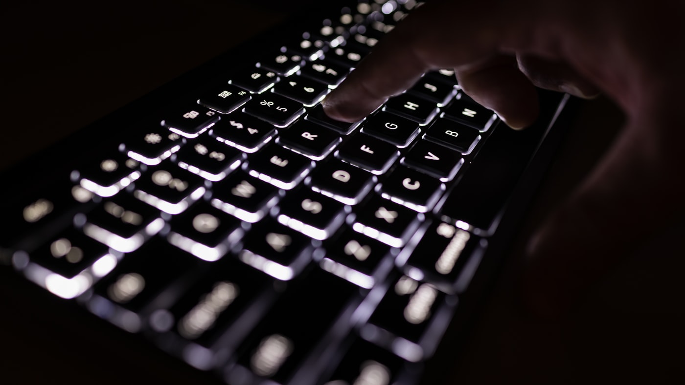 Mãos sobre um teclado retroiluminado em uma sala escura